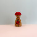 Wooden peg doll with a red hat and black and red design on a light gray background