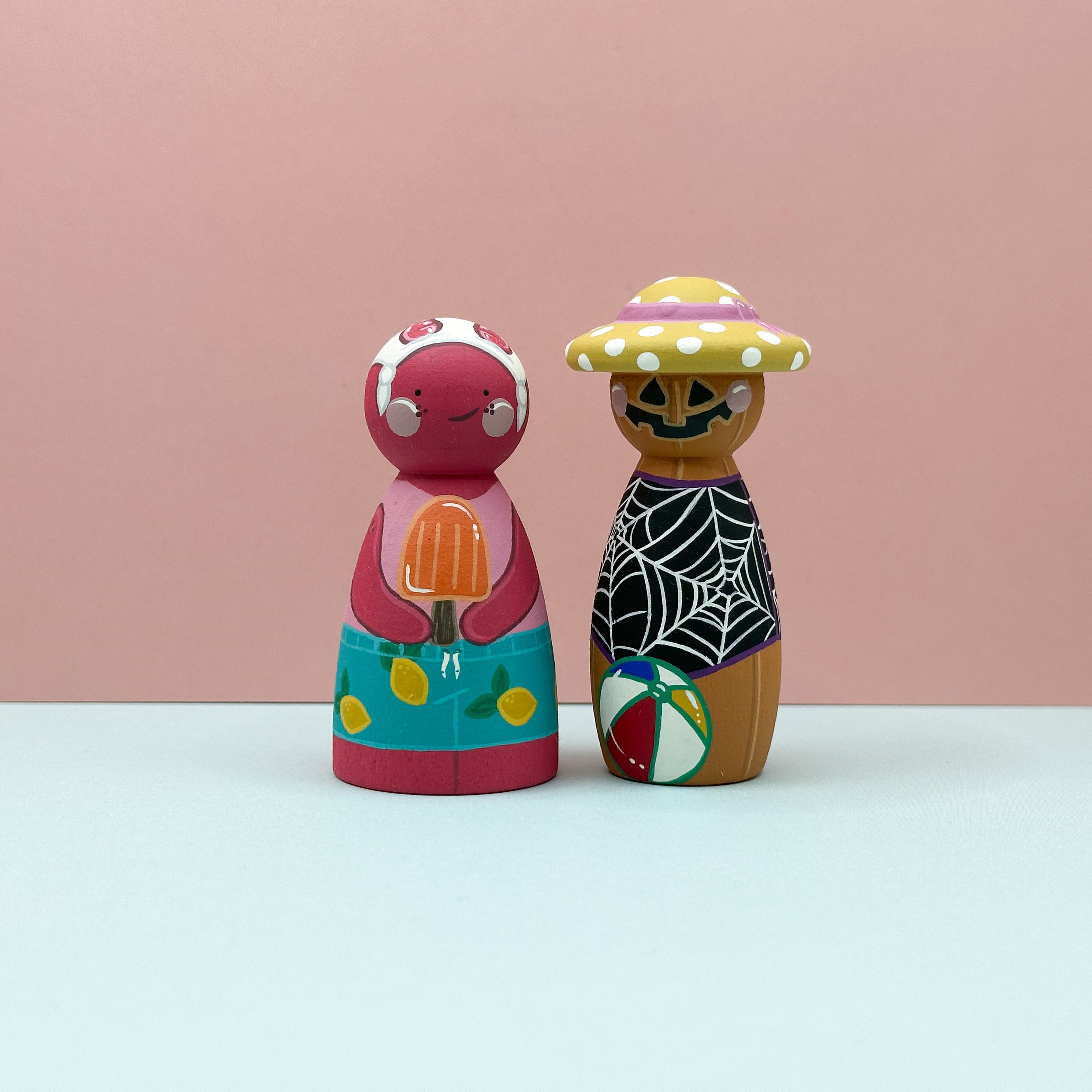 Two colorful wooden peg dolls on a light pink background