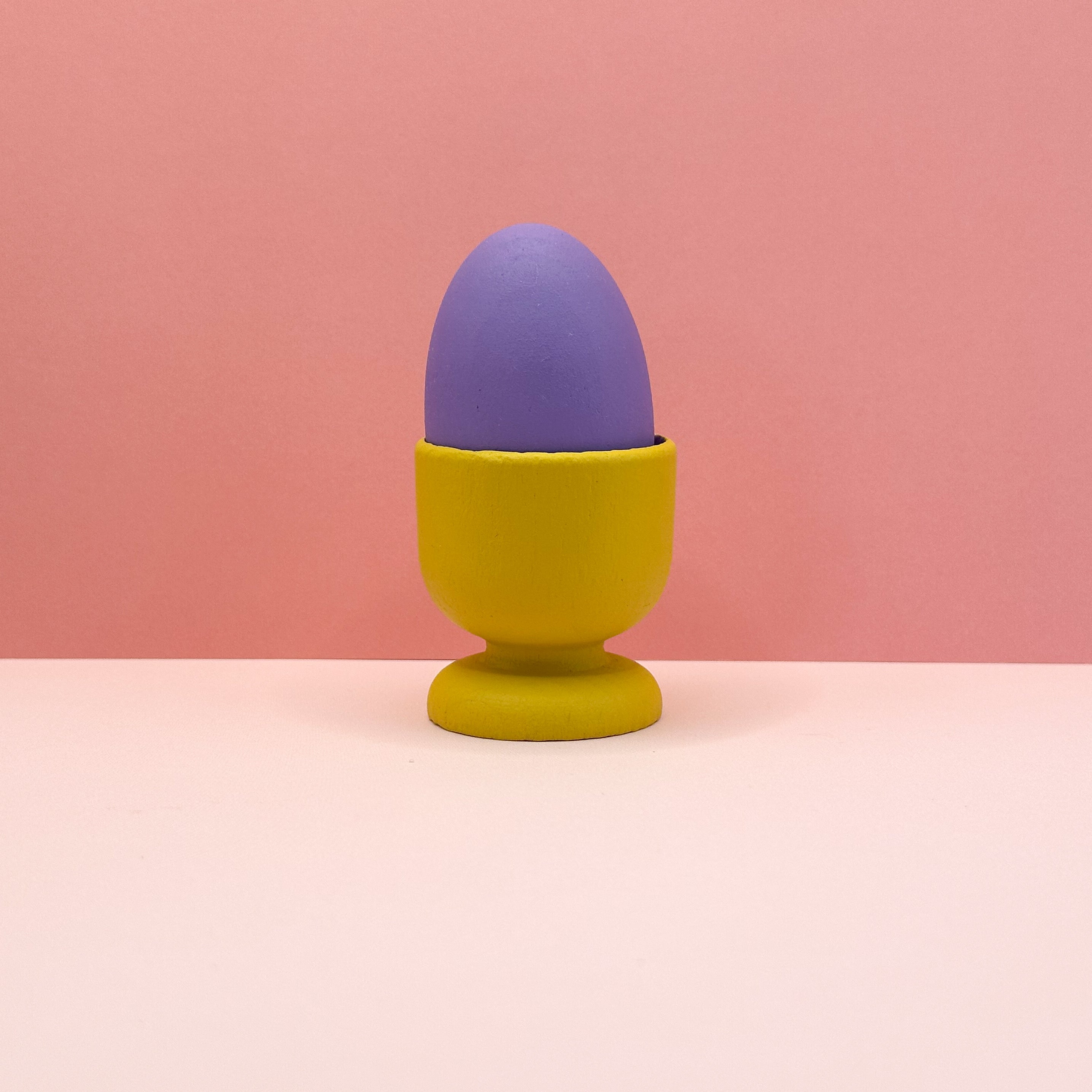 Purple egg in a yellow holder on a pink background
