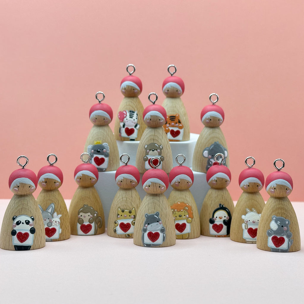 Little wooden pegdoll keyrings with various animals holding heart signs painted on their bodies on a peach background