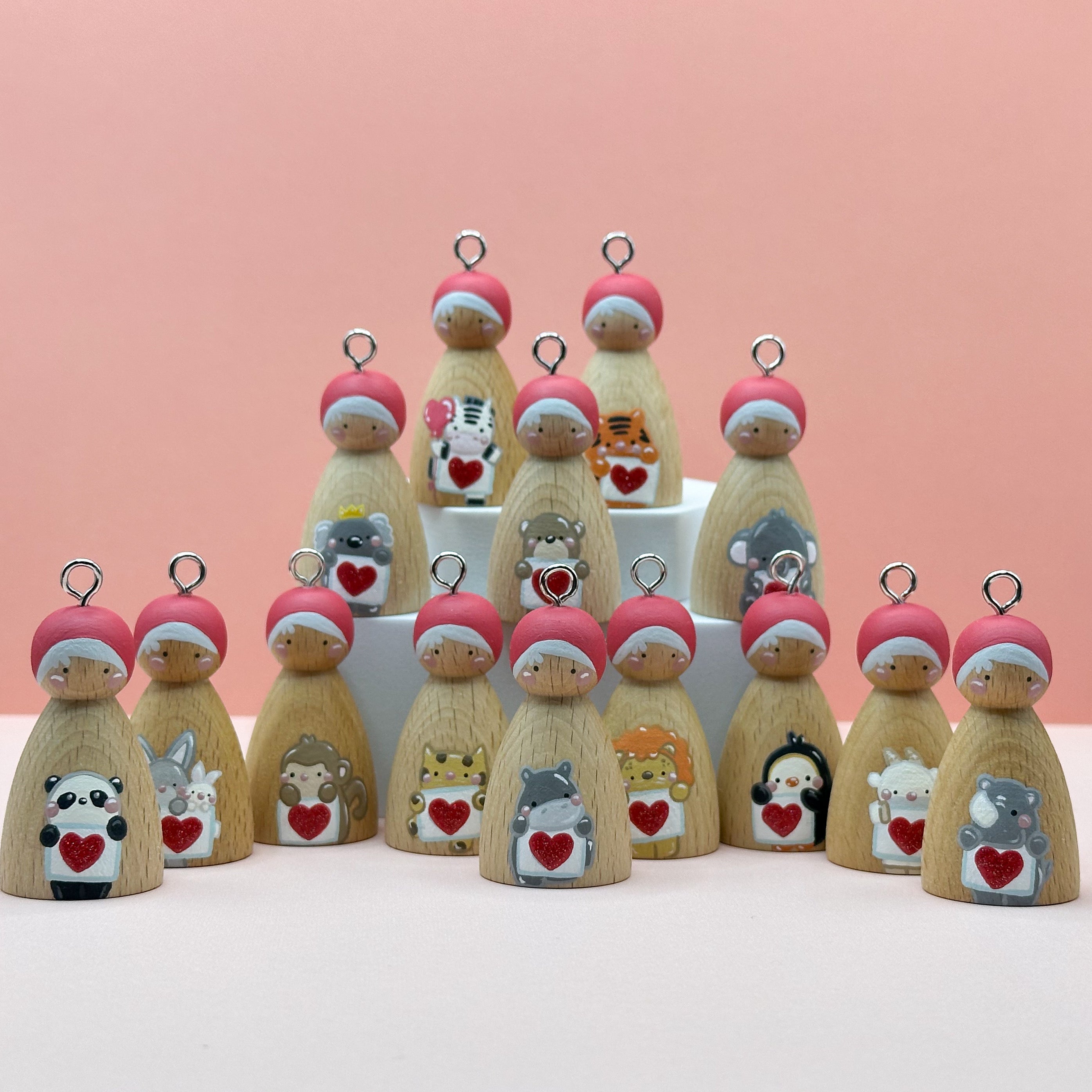 Little wooden pegdoll keyrings with various animals holding heart signs painted on their bodies on a peach background
