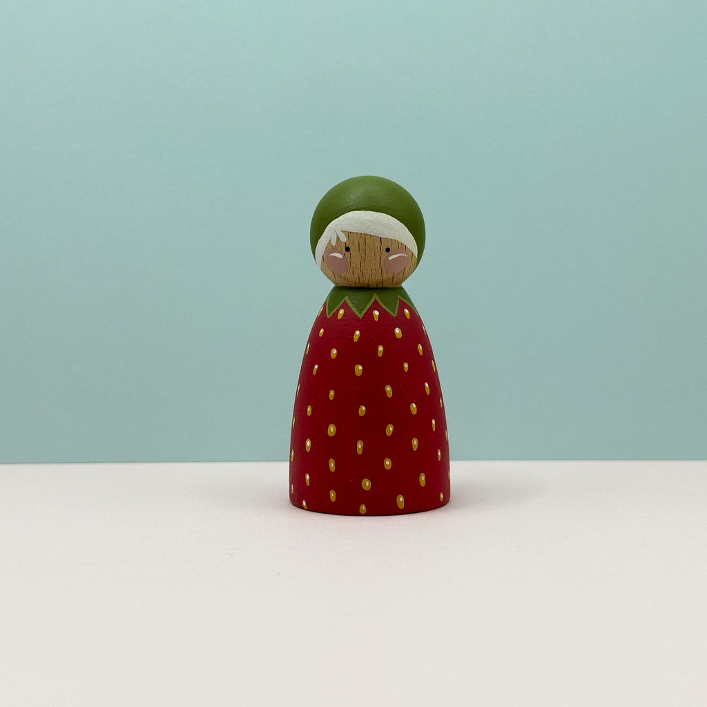 Wooden figurine shaped like a strawberry with a green top on a light blue background