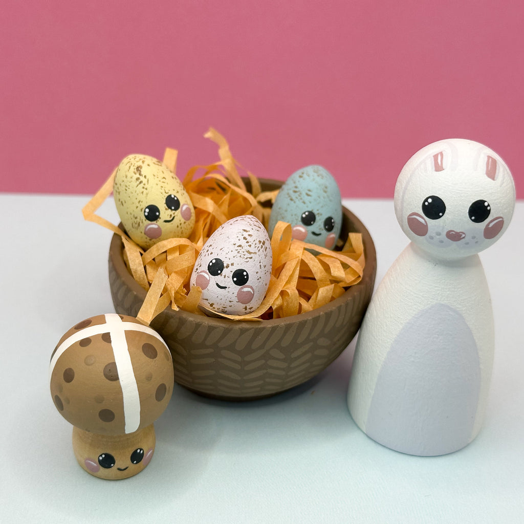 Decorative Easter eggs with faces in a wooden basket on a pink background