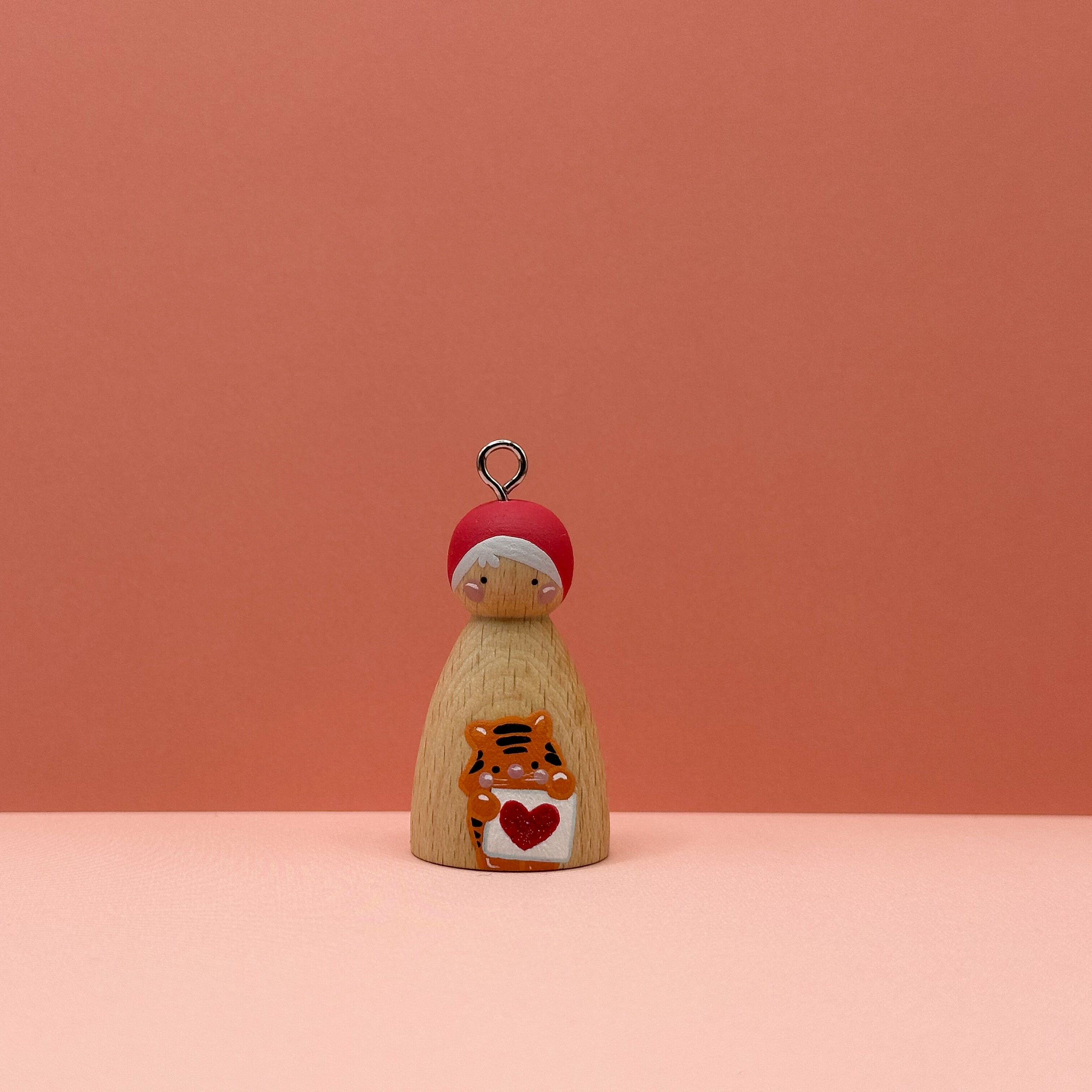 Small peg doll keyring with a tiger holding a heart sign painted on its body with a peach background