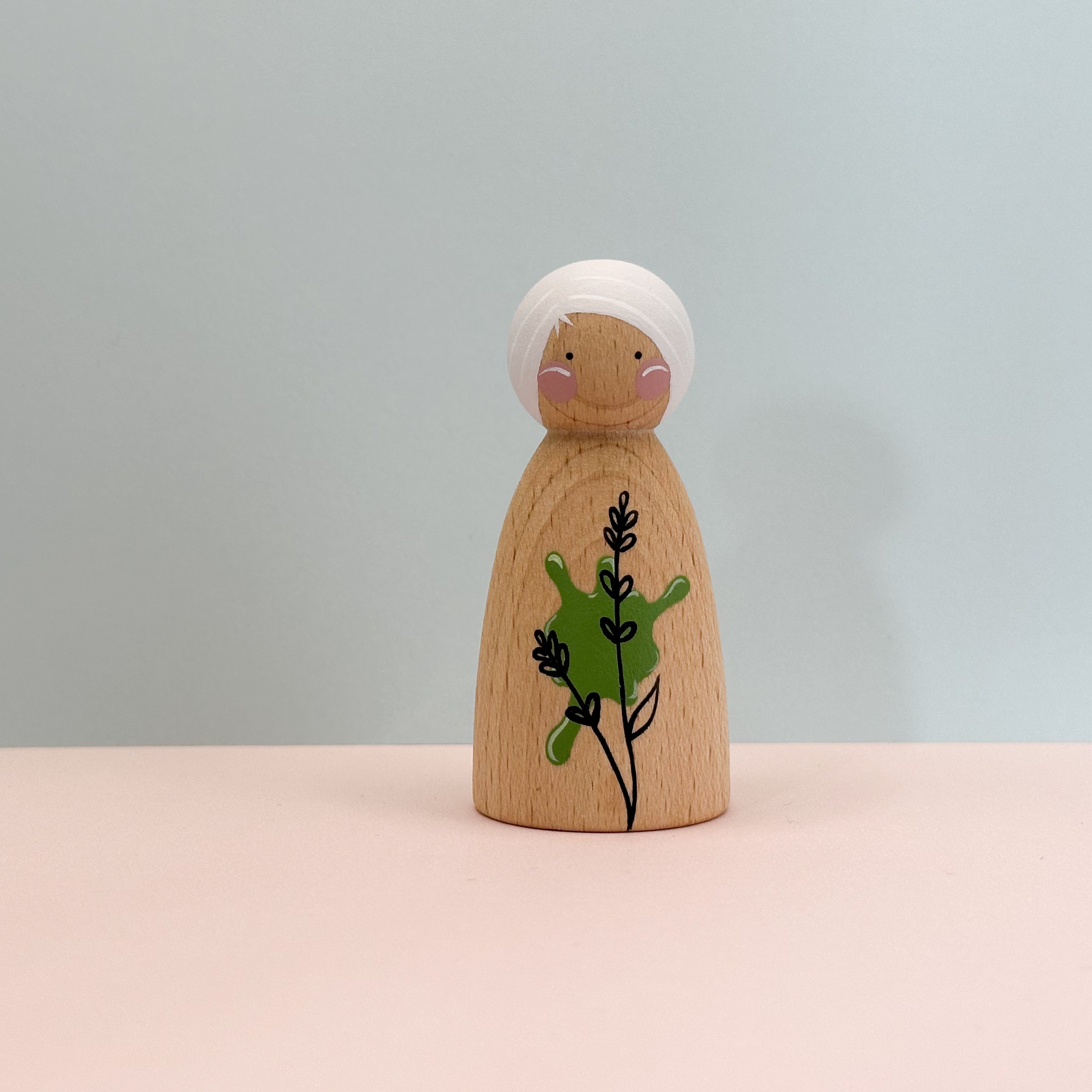 Wooden peg doll with white hair and green leaf design on a light gray background