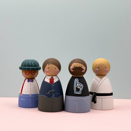 Four wooden peg dolls with different outfits on a light pink surface and gray background