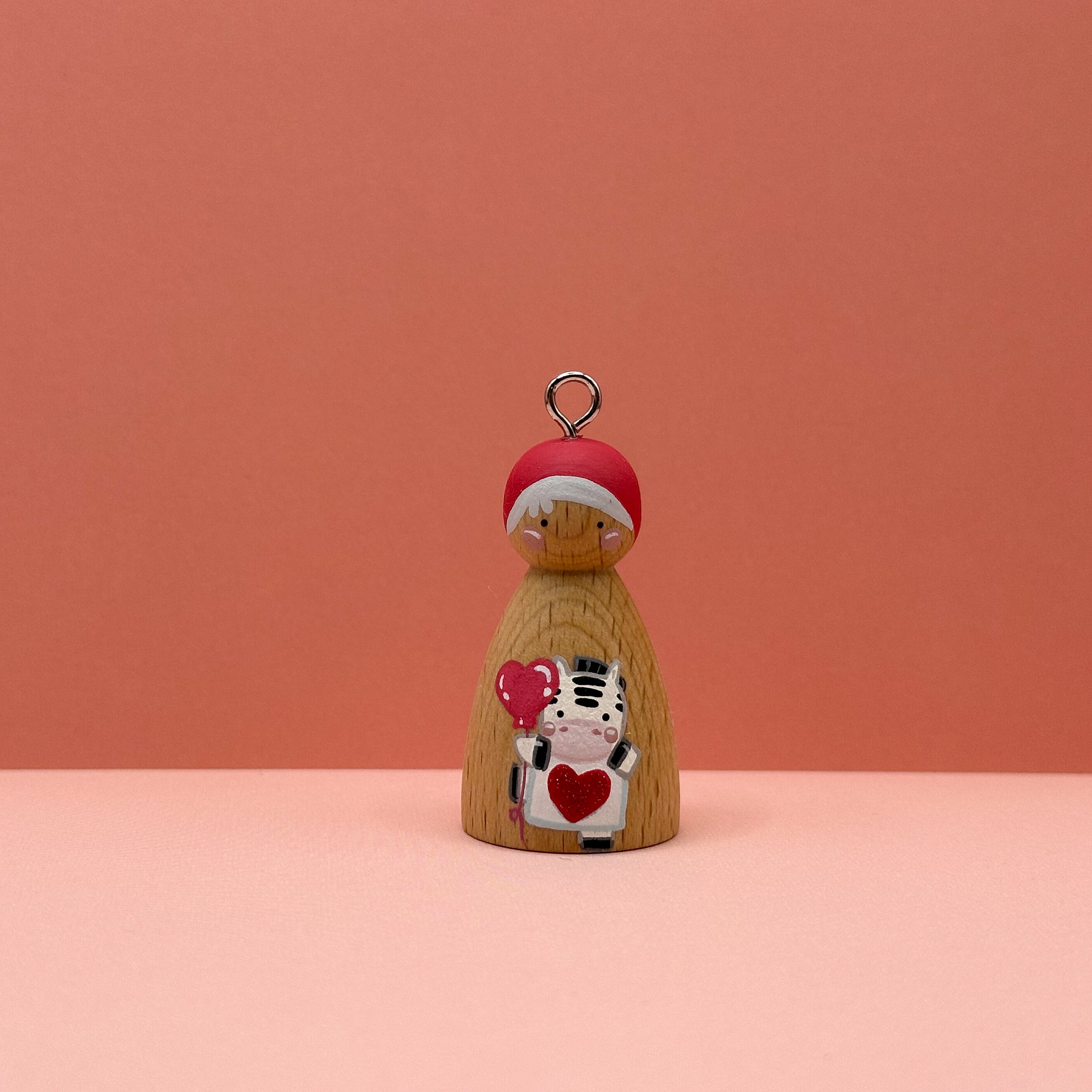 Small peg doll keyring with a zebra holding a heart sign painted on its body with a peach background