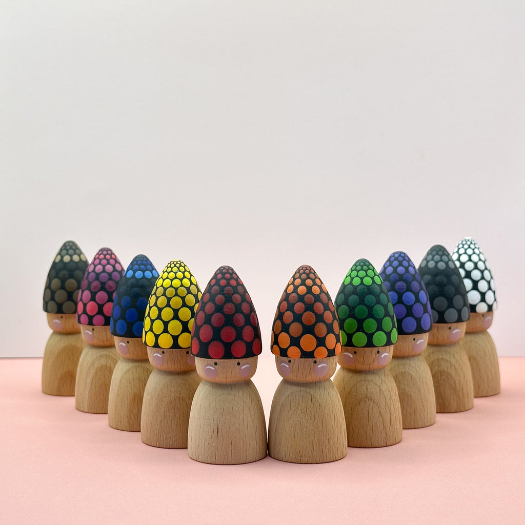Wooden peg dolls with colorful, patterned hats on a pink surface.