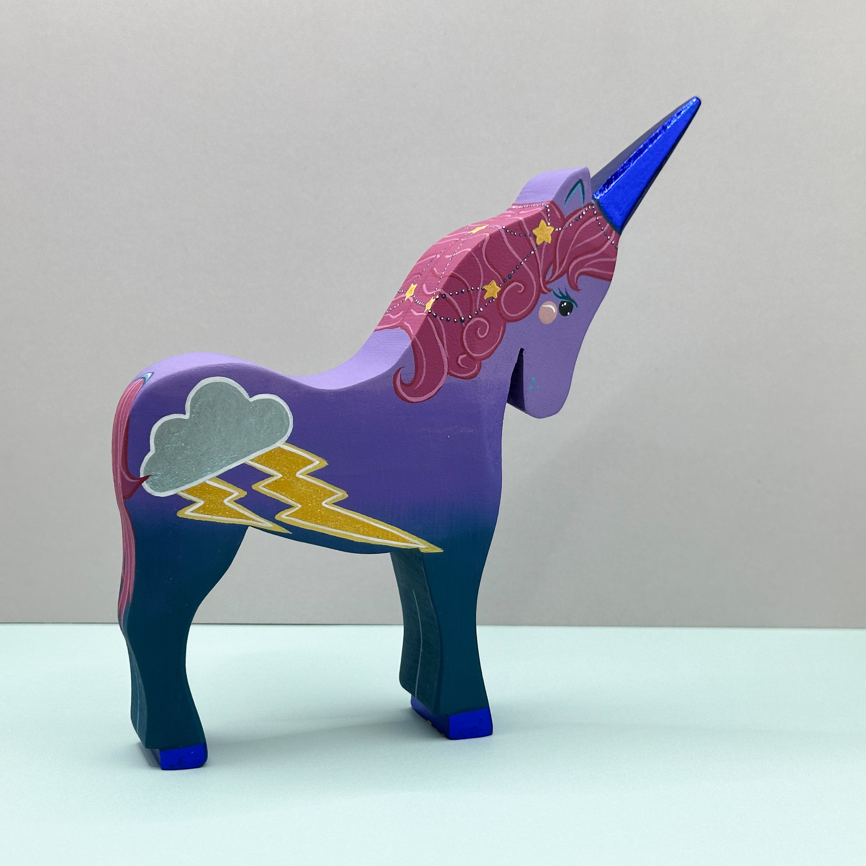 Colorful unicorn figurine with purple body, blue mane, and rainbow pattern on a light gray background