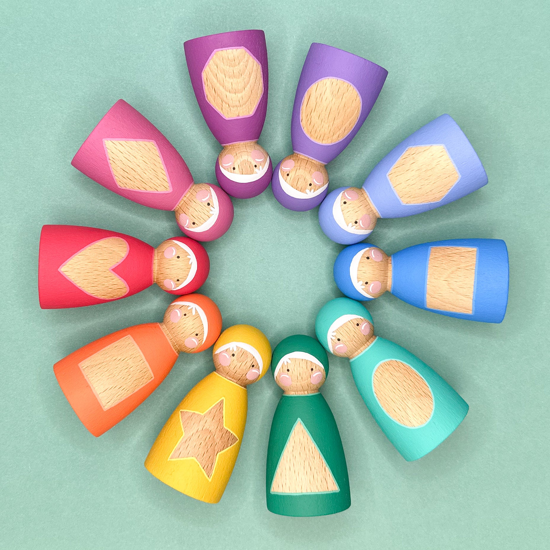 Colorful wooden dolls arranged in a circular pattern on a light green background. The dolls have shape patterns on their tummies. 