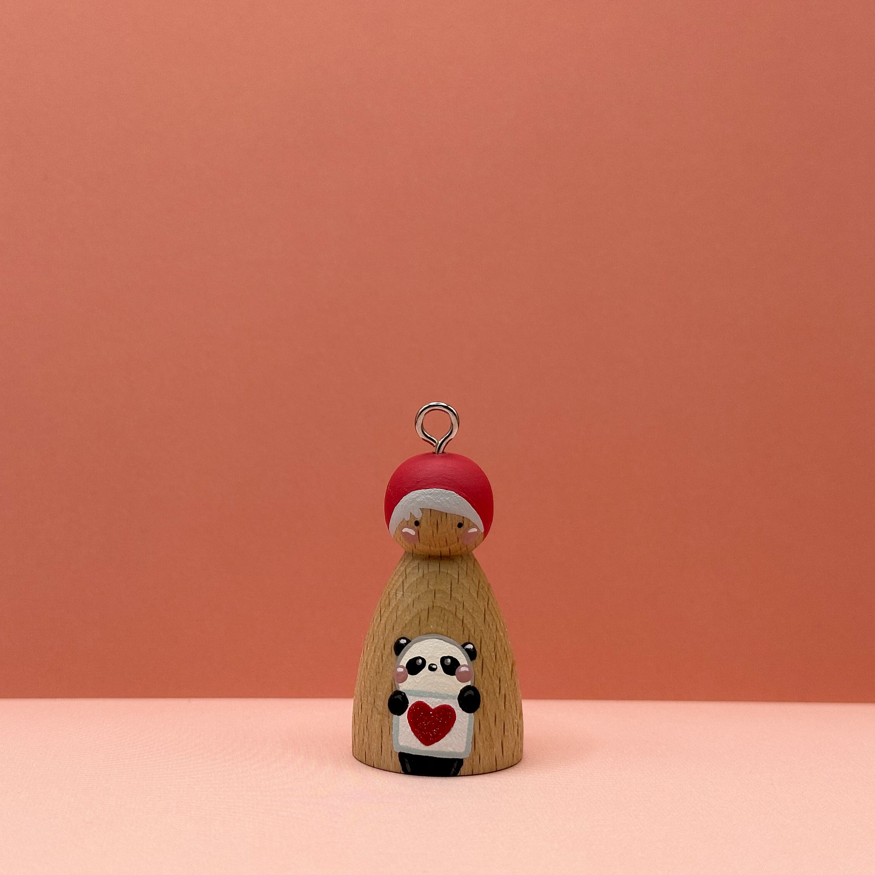 Small peg doll keyring with a panda holding a heart sign painted on its body with a peach background