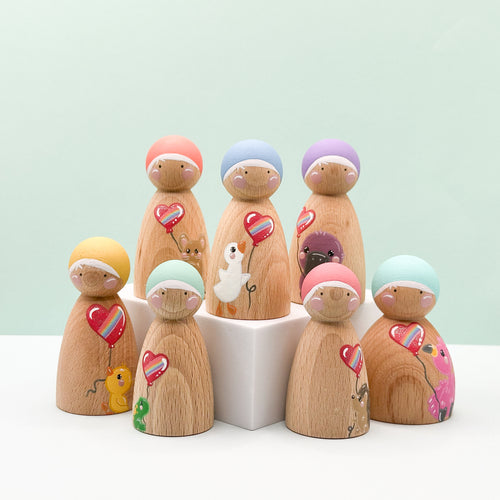 Wooden peg dolls with colorful hats and heart-shaped balloons on a light green background