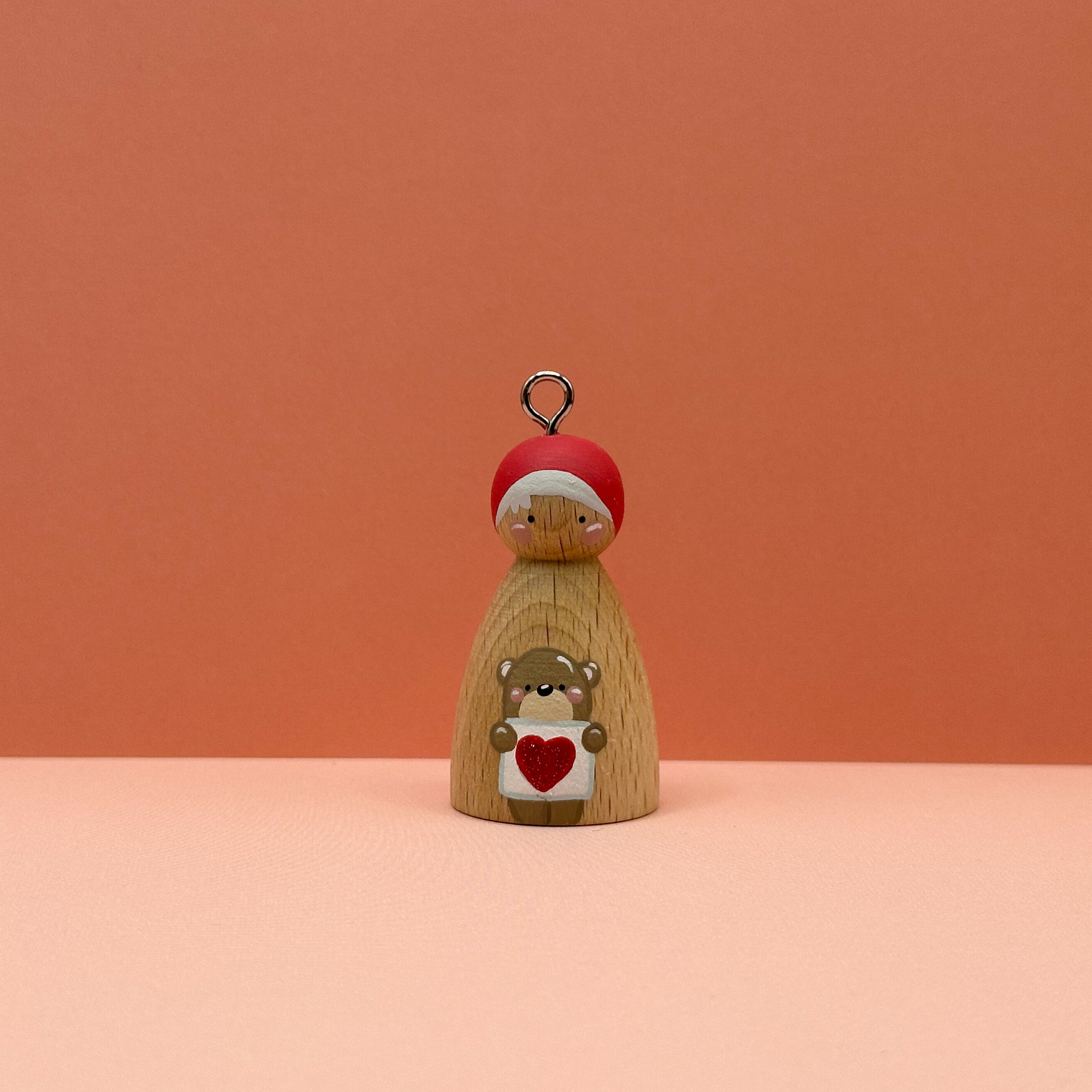 Small peg doll keyring with a bear holding a heart sign painted on its body with a peach background