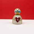 a chubby wooden peg doll dressed as a bear holding a love heart on a red background