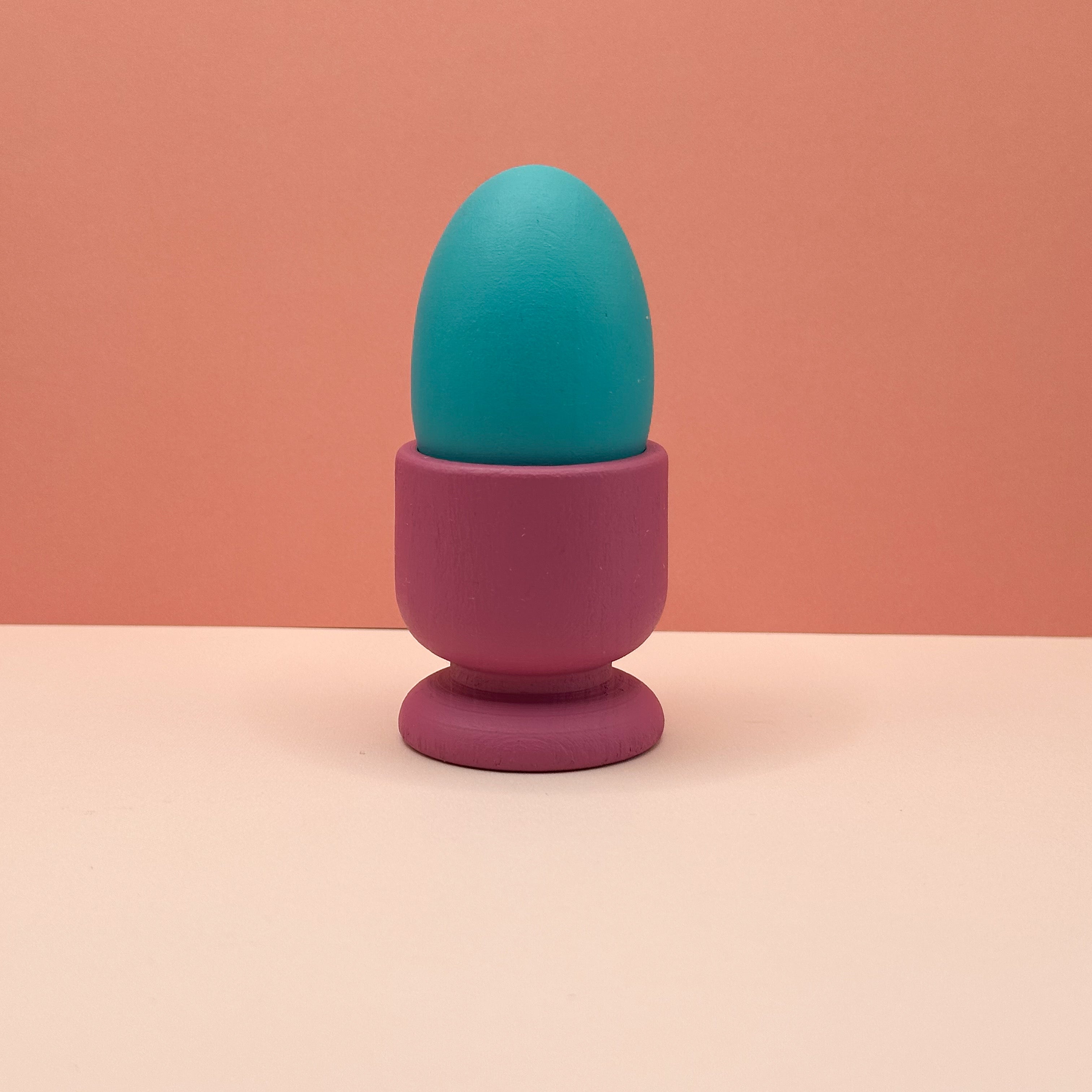 Turquoise egg in a pink holder on a peach background