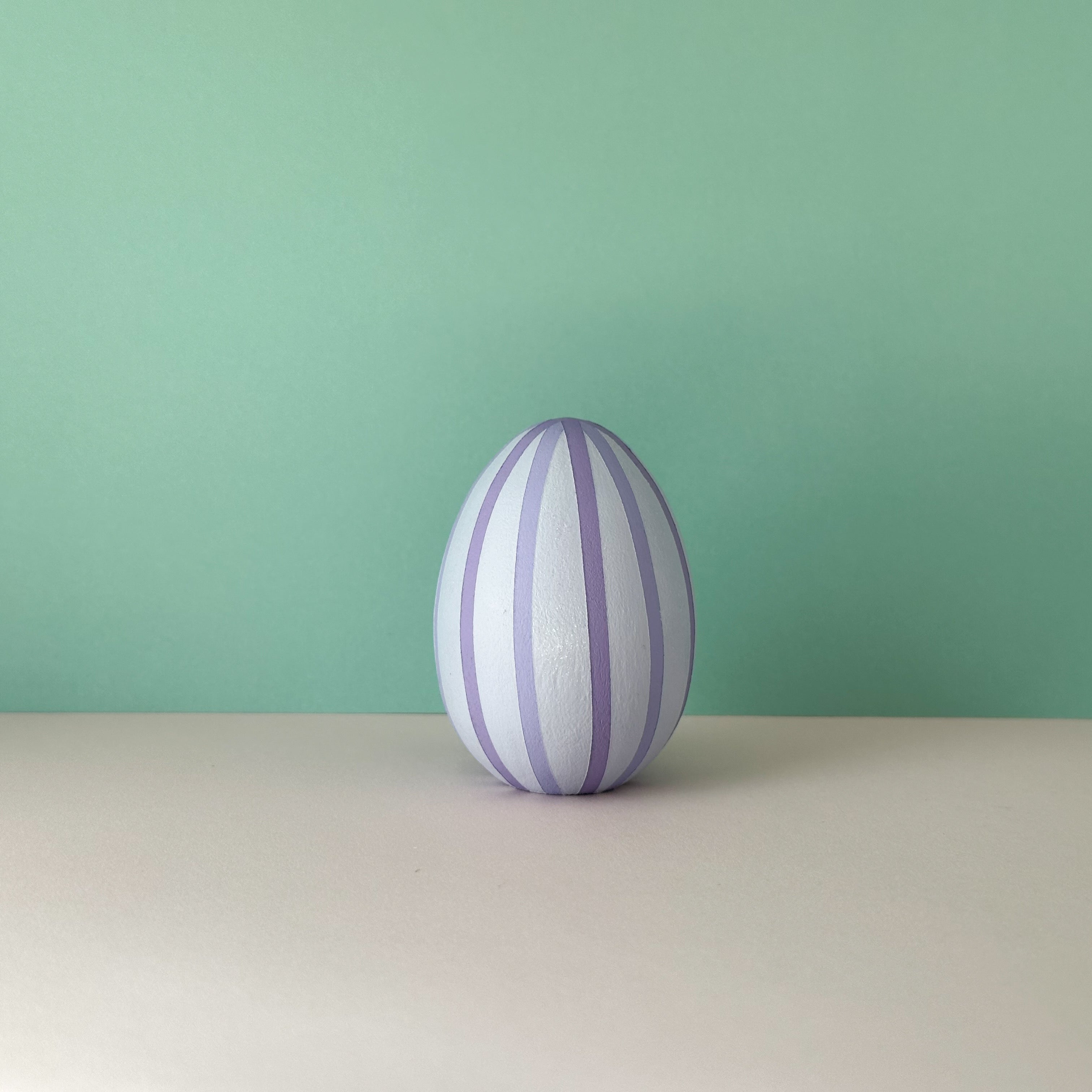 Egg-shaped object with purple stripes on a light surface and green background
