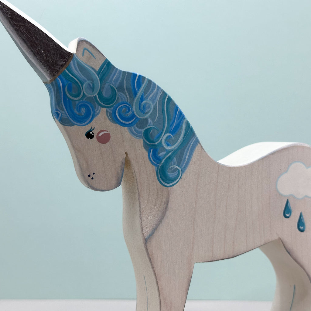 Wooden unicorn figurine with blue mane and cloud design on a light blue background