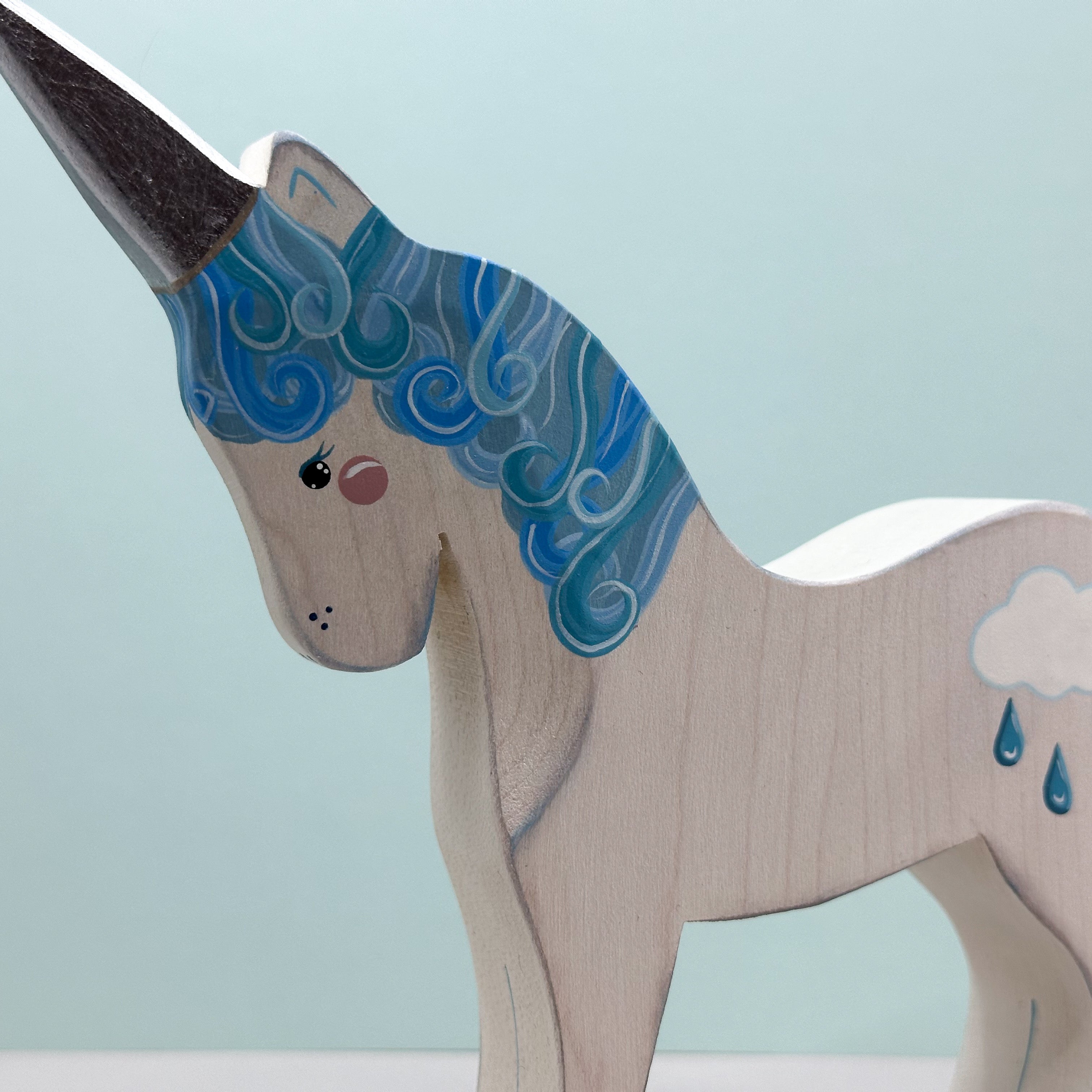 Wooden unicorn figurine with blue mane and cloud design on a light blue background