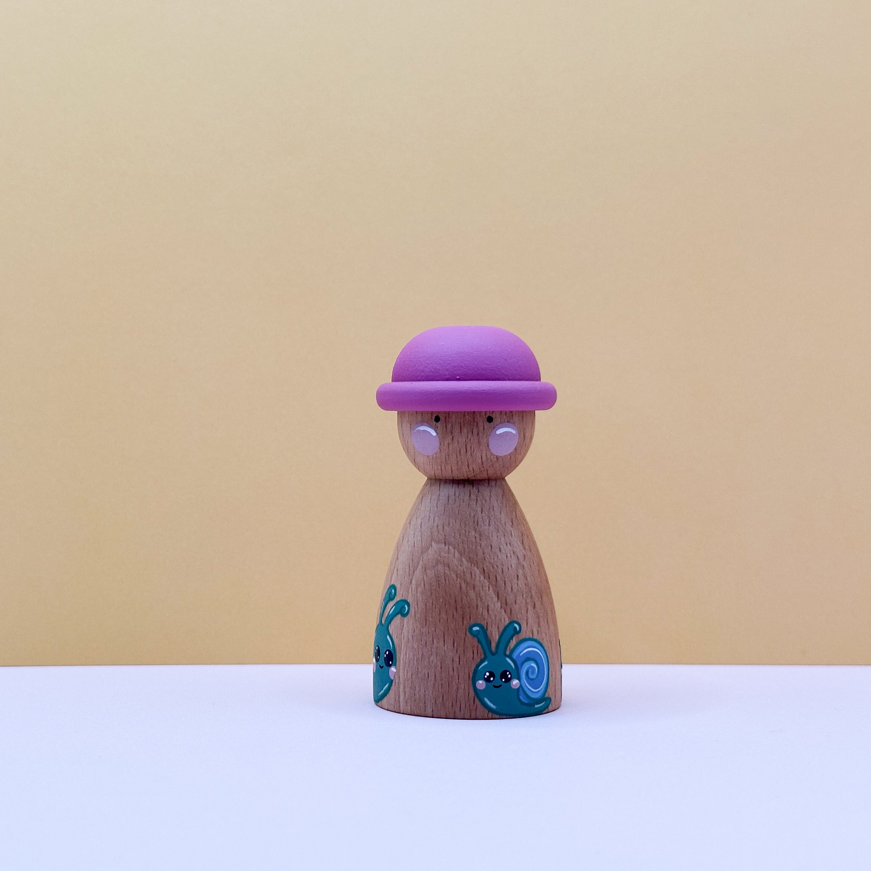 Wooden peg doll with a pink hat on a beige background