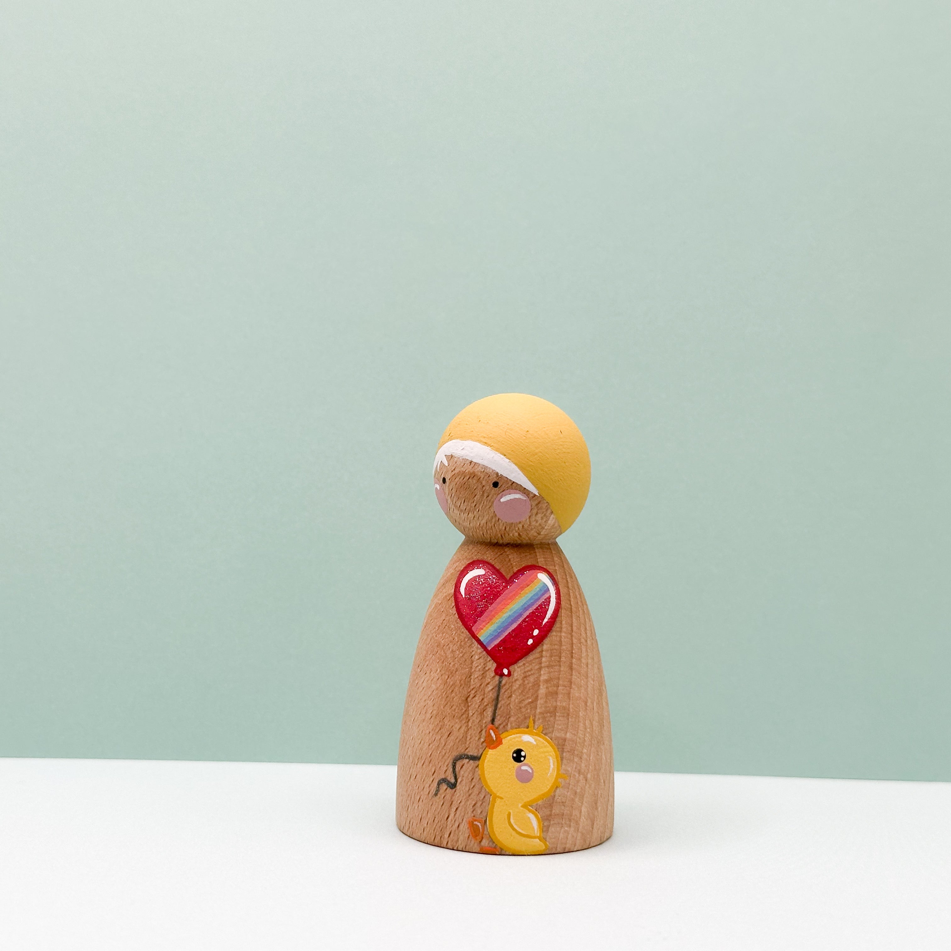 Wooden figurine with a heart-shaped balloon and a duck on a light green background