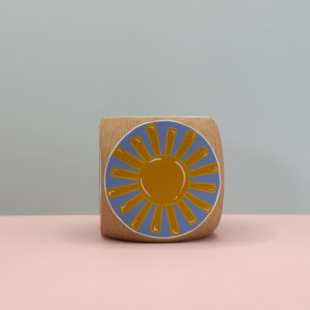 Wooden block with a sun design on a pink surface and gray background