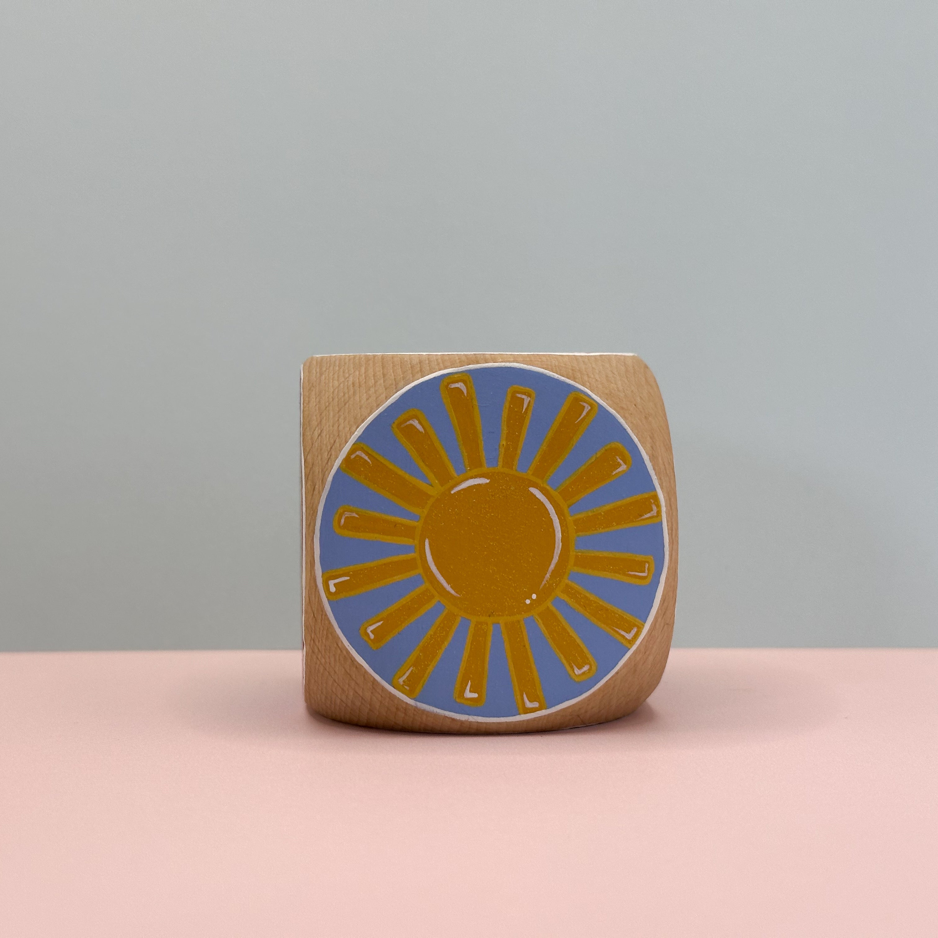 Wooden block with a sun design on a pink surface and gray background