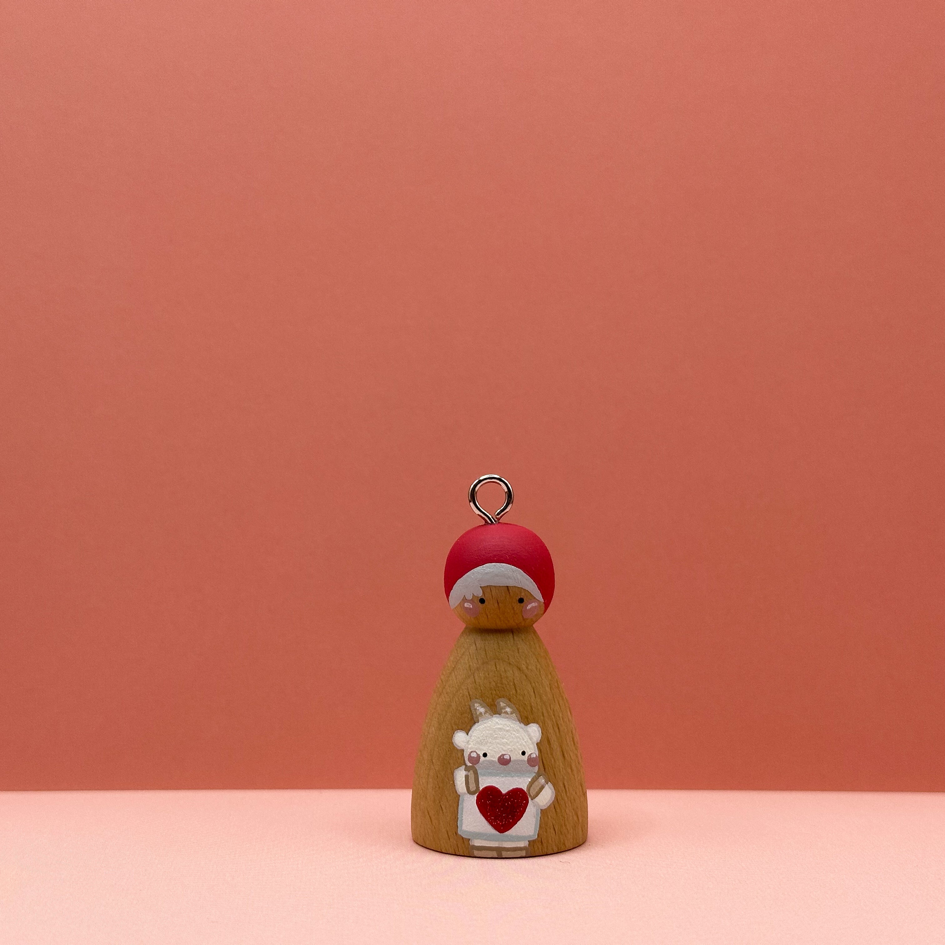 Small peg doll keyring with a goat holding a heart sign painted on its body with a peach background