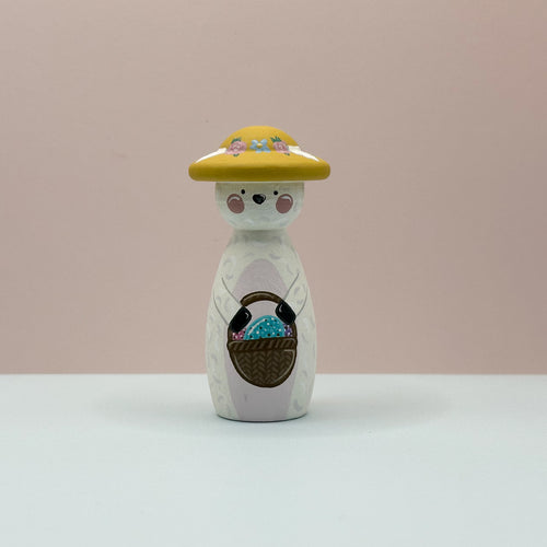 Wooden figurine with a yellow hat and basket on a light pink background