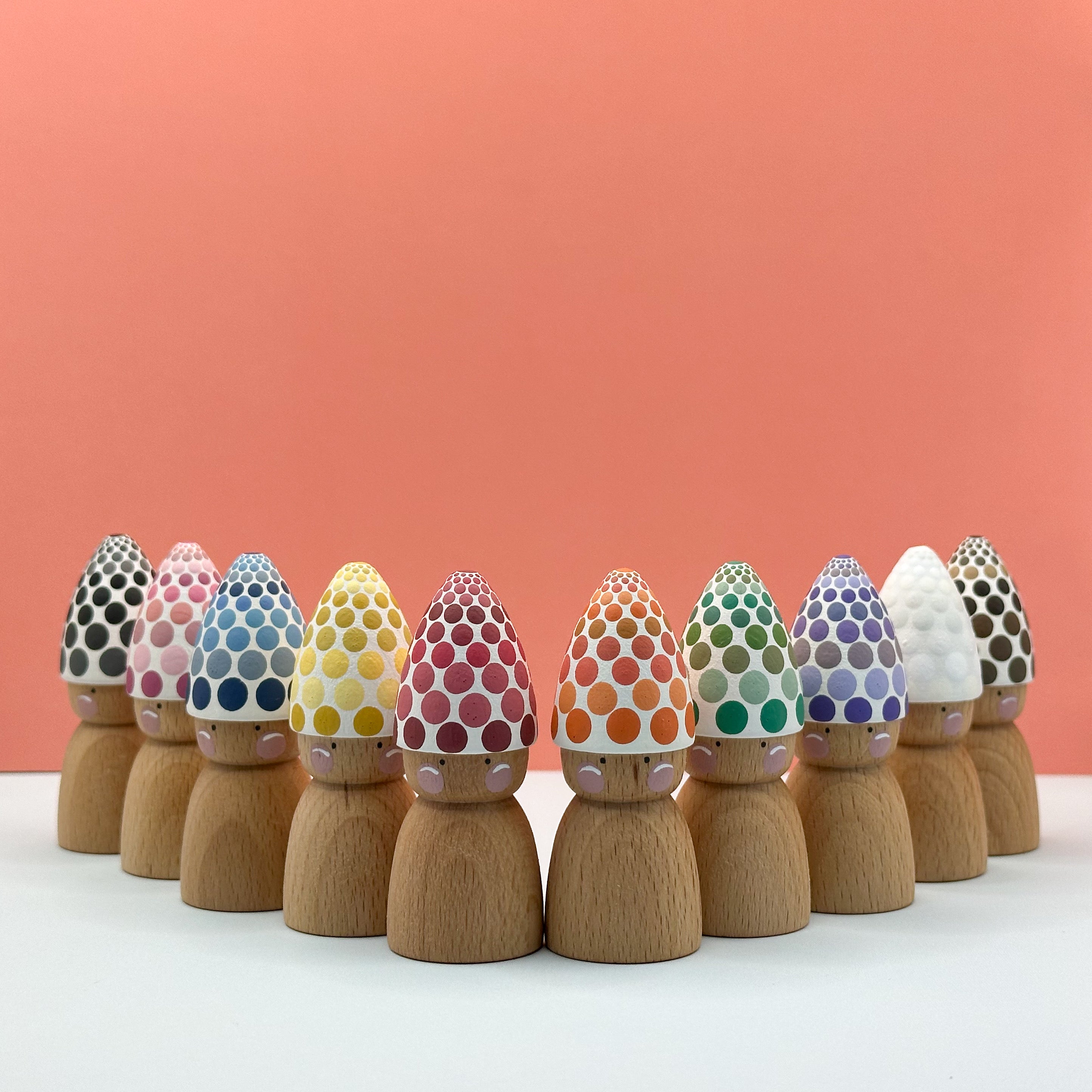 Wooden peg dolls with colorful dot hats on a white surface and peach background