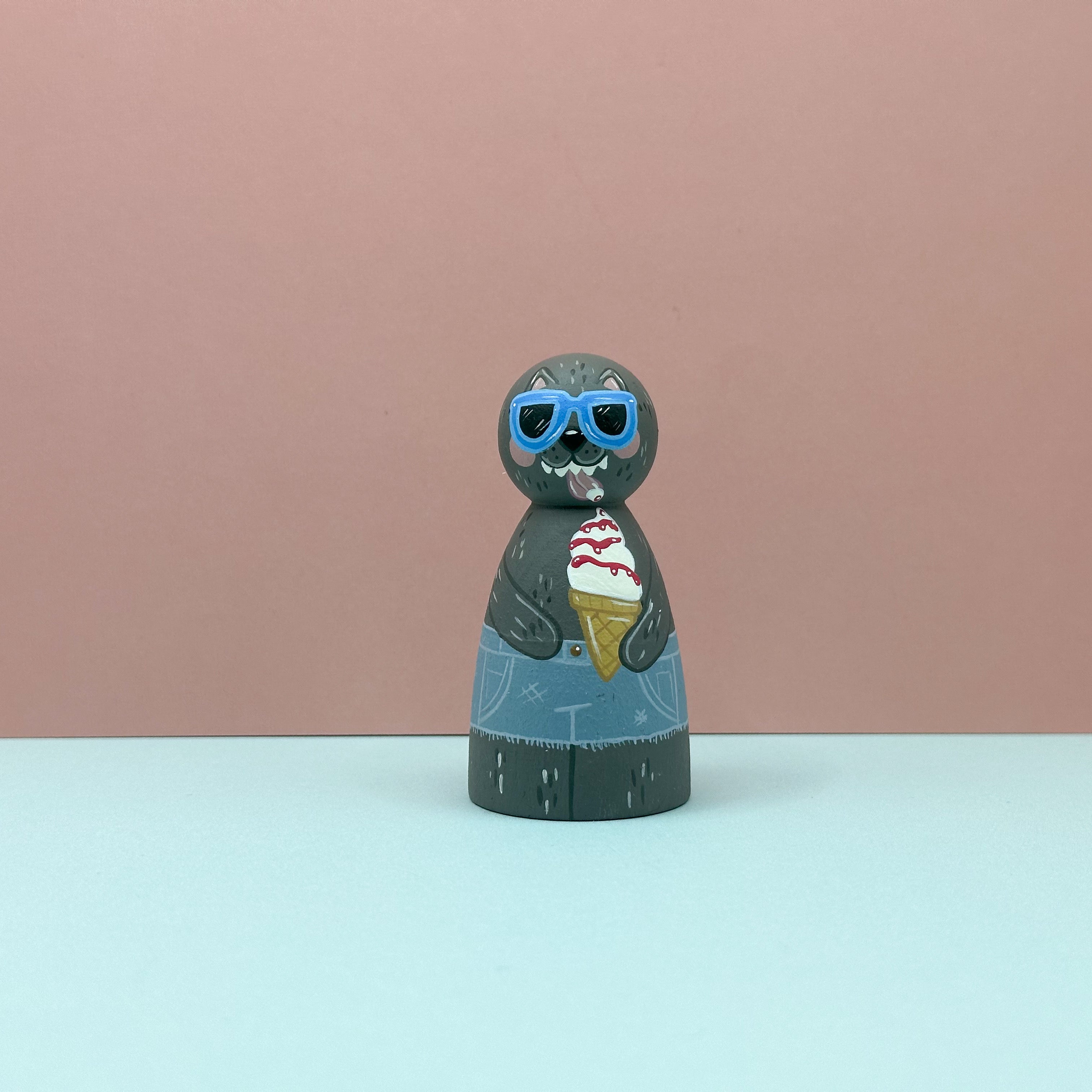 Figurine of a wolf wearing sunglasses and holding an ice cream cone on a pink and blue gradient background