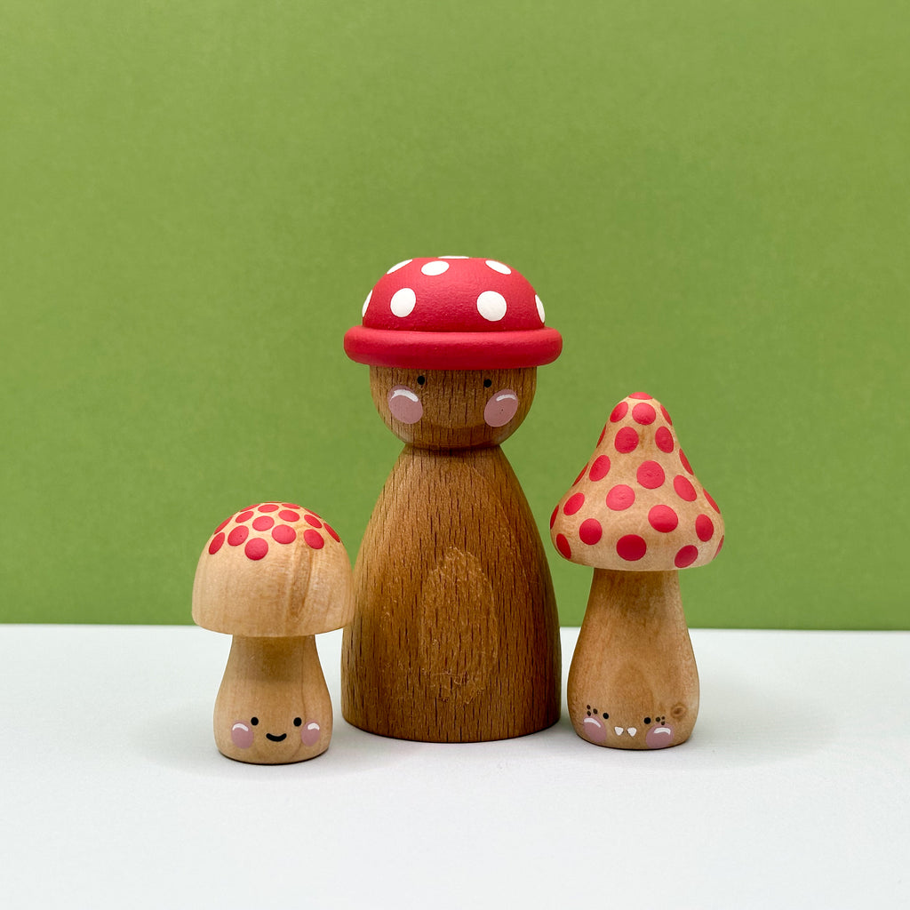 Wooden figurines resembling a mushroom family with red polka dot hats on a green background