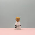 Wooden figure of a person in a kimono with a black belt on a pink and gray background