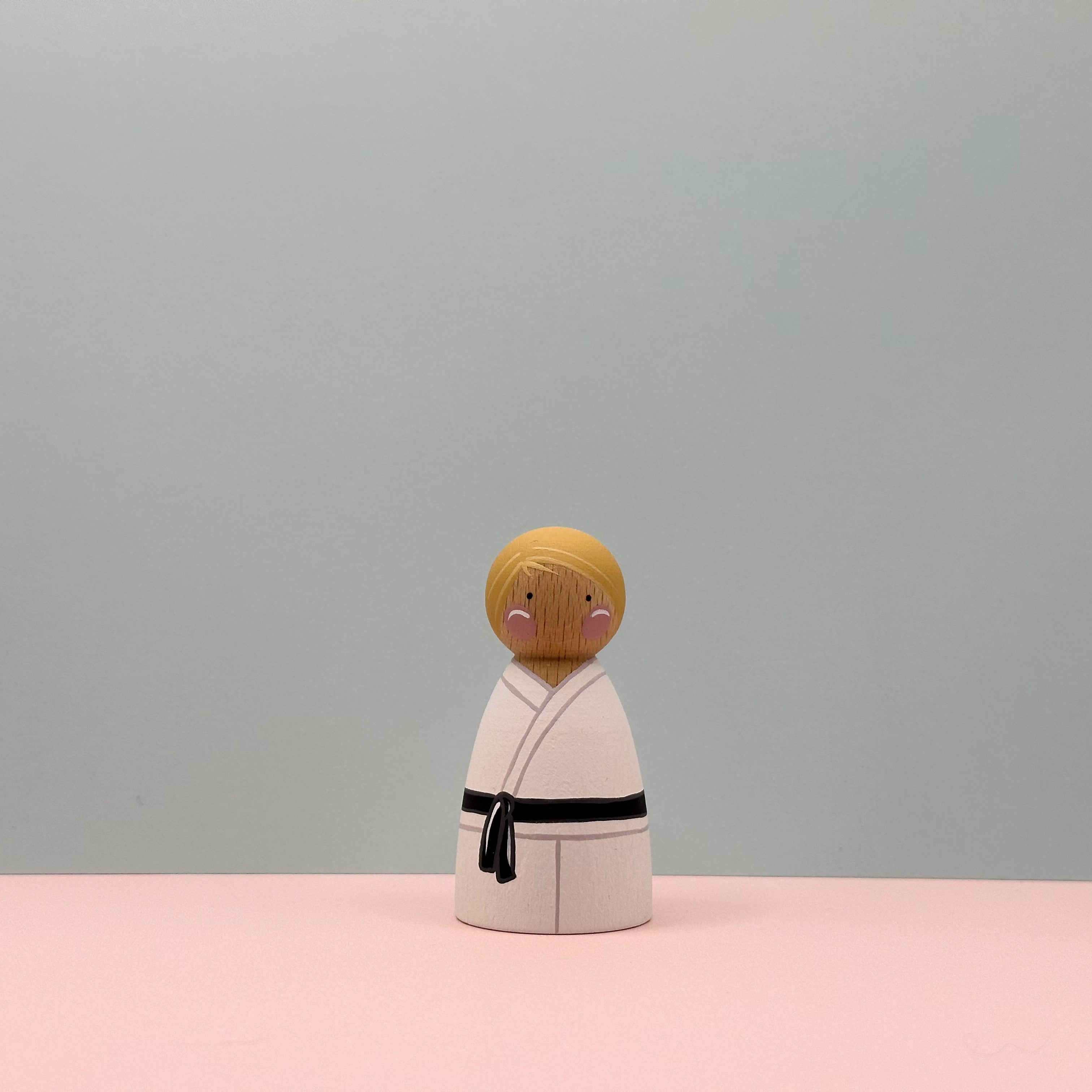 Wooden figure of a person in a kimono with a black belt on a pink and gray background
