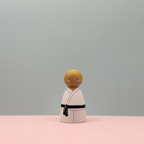 Wooden figure of a person in a kimono with a black belt on a pink and gray background