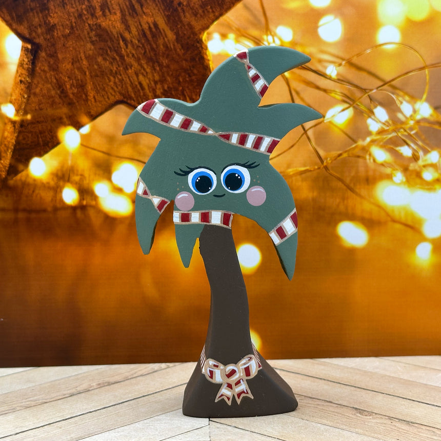 Decorative palm tree figurine with candy cane ribbbon on a wooden surface with blurred lights in the background