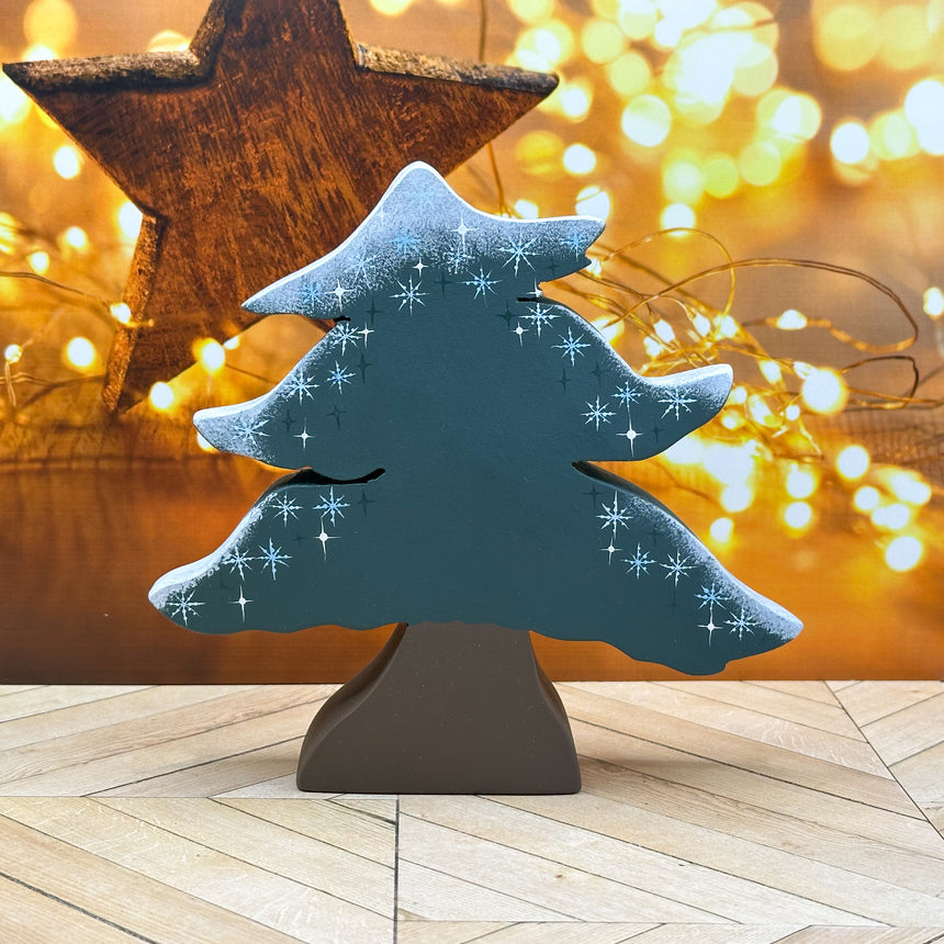 Decorative Christmas tree with snowflakes on a wooden stand against a warm, blurred background.