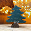 Decorative Christmas tree figurine with a happy face on a wooden surface with blurred lights in the background.