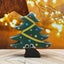 Decorative Christmas tree figurine with colorful dots on a wooden surface with blurred lights in the background.
