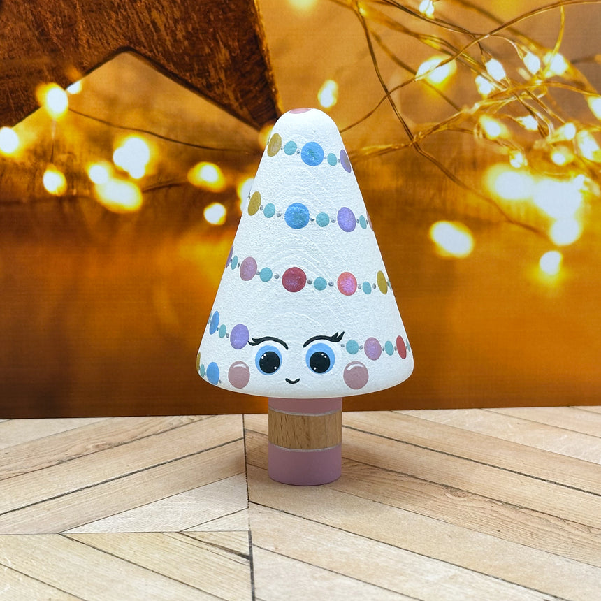 Decorative Christmas tree toy with a cartoon face on a wooden floor with blurred lights in the background