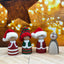 Four Christmas-themed figurines with festive hats on a wooden surface with blurred lights in the background.