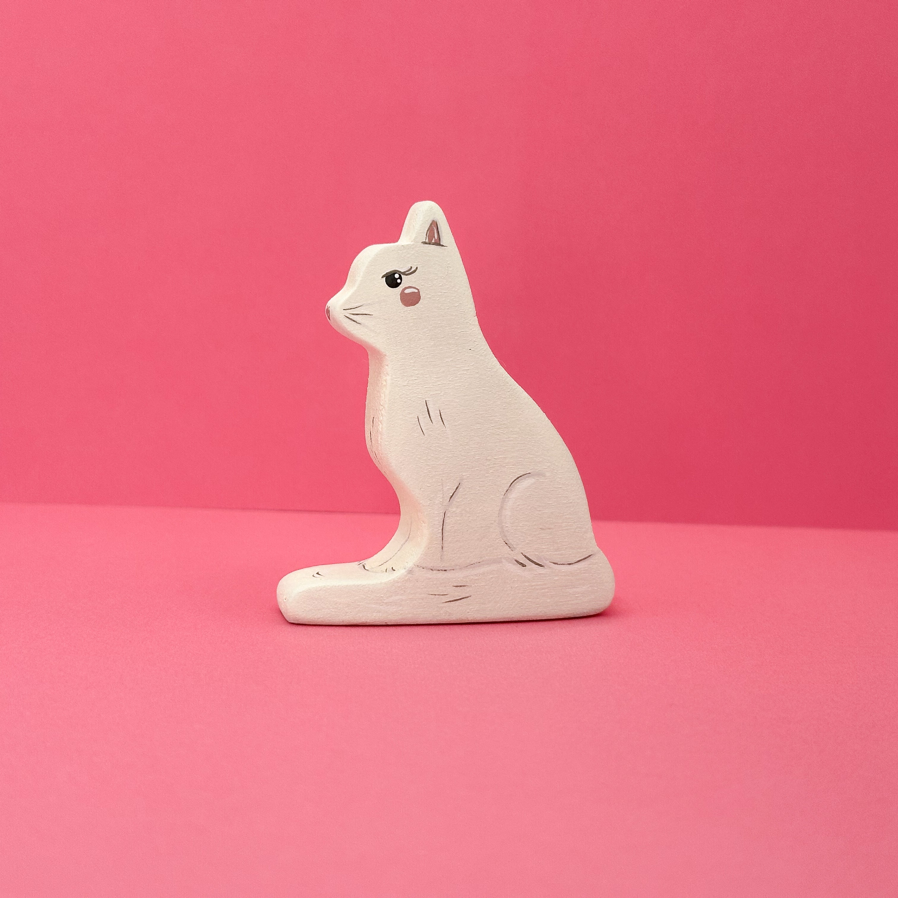White wooden cat figurine on a pink background
