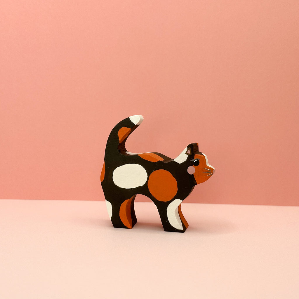 Wooden cat figurine with a tortie pattern on a pink background