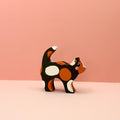Wooden cat figurine with a tortie pattern on a pink background